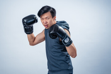 Asian man in sleeveless hoodie wearing boxing gloves throws forward punch with intense facial...