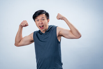 Asian man in sleeveless hoodie flexing both arms and shouting excitedly with energetic facial...