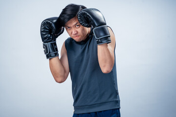 Asian man in sleeveless hoodie wearing boxing gloves throws forward punch with intense facial...
