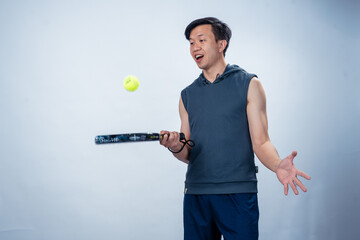 Asian man in sleeveless hoodie and shorts holding padel racket prepares for swing with focused face...