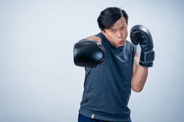 Asian man in sleeveless hoodie wearing boxing gloves throws forward punch with intense facial...