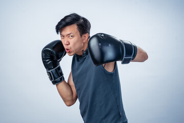 Asian man in sleeveless hoodie wearing boxing gloves throws forward punch with intense facial...