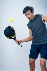 Asian man in sleeveless hoodie and shorts holding padel racket prepares for swing with focused face...