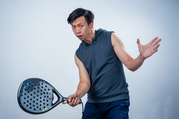 Asian man in sleeveless hoodie and shorts holding padel racket prepares for swing with focused face...