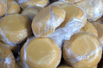 Wrapped Palm Sugar Discs. Close-up view of traditional Thai palm sugar discs wrapped in clear plastic, neatly stacked for sale at a local market.