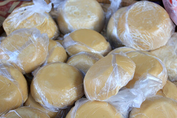 Palm Sugar Piled in Bulk. A large pile of wrapped round palm sugar discs displayed in a traditional Thai market basket.