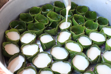 Pouring Coconut Milk into Banana Leaf Cups. A step in Thai dessert preparation where sweet coconut...