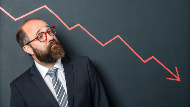 Businessman suit glasses beard red arrow downward trend chalkboard financial crisis concern economics. Inflation ,stagflation, recession and depression . Economic, financial crisis concept