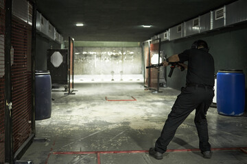 Fototapeta premium Man practicing shooting with rifle at indoor gun range standing in firing position aiming at paper targets in distance during training session