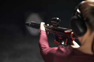 Young unrecognizable woman wearing protective earmuffs aiming rifle at shooting range, focusing on...