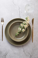 Top view of olive green tableware, golden cutlery and glass goblet on a light cement surface. White...