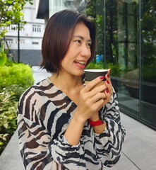 Beautiful Asian woman in a dress holds a paper cup of coffee, embracing an eco-conscious urban lifestyle
