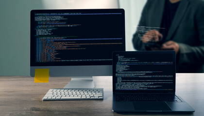 Programming code on representing Close up of computer monitor and laptop displaying code, with person background using tablet, modern workspace