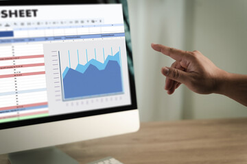 Man working on excel person pointing at computer screen displaying spreadsheet and line graph, analyzing data and trends in professional setting