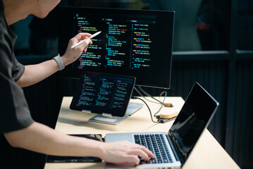 Male programmer using stylus to analyze code on tablet and monitor. Software development, coding, and tech workspace concept