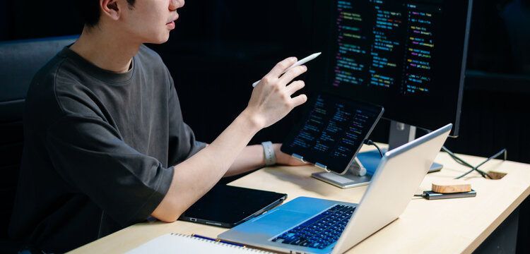 Male programmer using stylus to analyze code on tablet and monitor. Software development, coding, and tech workspace concept