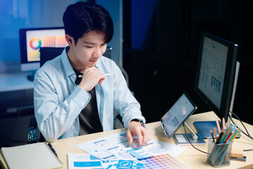 Asian UX,UI designer reviewing app wireframes and color samples in modern office. Creative process,...