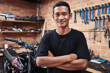 Indonesian male motorcycle mechanic smiling proudly in his workshop after finishing a job
