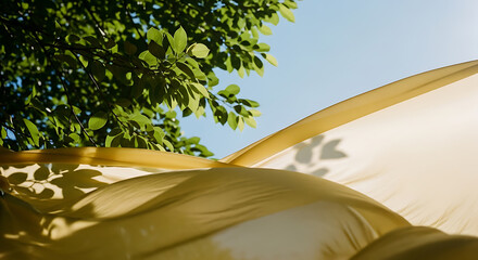 Sunlit Golden Fabric Billowing with Tree Leaf Shadows Against Blue Sky and Green Foliage