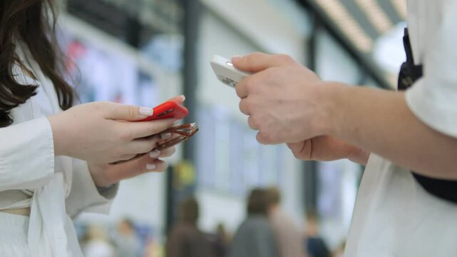 Two people are looking at their phones in a busy area. One of them is holding a red phone