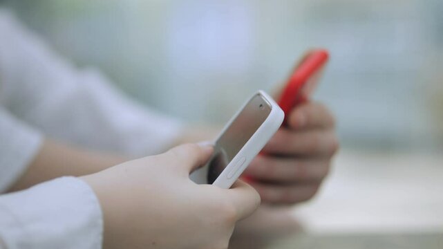 Person is holding a cell phone with a white case and a red band. The person is looking at the phone, possibly texting or browsing the internet. Concept of modern technology and communication
