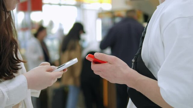 Two people are looking at their phones in a store. One of them is holding a red phone
