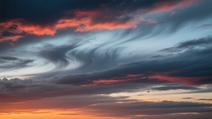 Fototapeta premium Dramatic sky with swirling clouds in shades of gray and orange at the horizon during sunset time