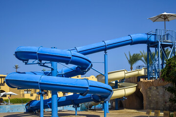 Fototapeta premium Water attraction, spiral slides in courtyard of cozy Egyptian hotel with palms. Transparent clean water, blue sky. Eastern architecture. Ideal place, active recreation area. No people. Copy space.