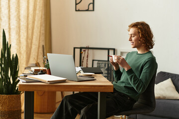 Young man enjoying a warm drink while relaxing at his cozy home workspace during a sunny afternoon