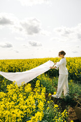 Woman in white outfit spreads fabric in vibrant yellow flower field on a sunny day