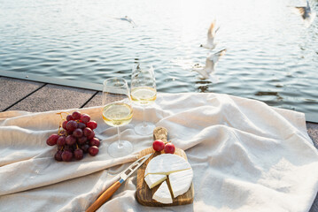 Two glasses of white wine with cheese and grapes on a pier at sunset.
