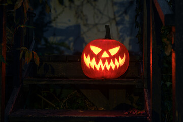 Carved pumpkin with inner glow stands outdoor. Halloween holiday concept with eerie lighting and cozy fall arrangement