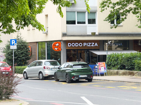 Ljubljana, Slovenia - June 03, 2025: Dodo Pizza restaurant exterior view with parked cars on the street, showcasing vibrant signage and urban atmosphere in a lively neighborhood