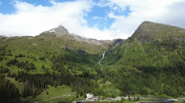 Aerial shot of alpine valley with waterfall and remote building infrastructure.