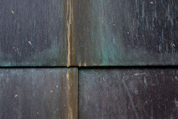 Close-up of weathered copper or bronze panels with oxidation, rust streaks, and patina in green,...