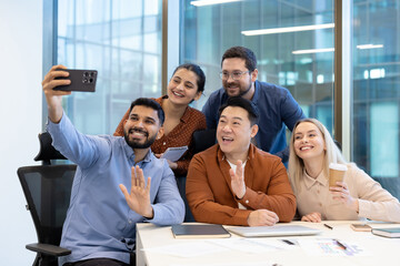 A diverse group of colleagues taking a selfie together in a modern office setting, showcasing...