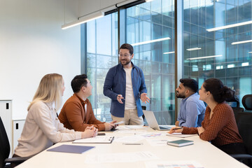 A diverse team collaborates in a modern office setting during a business meeting. They are discussing a plan.