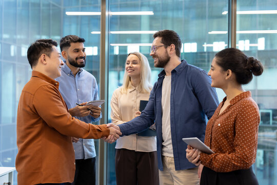 Diverse business team members shake hands in a modern office setting, symbolizing agreement and collaboration.