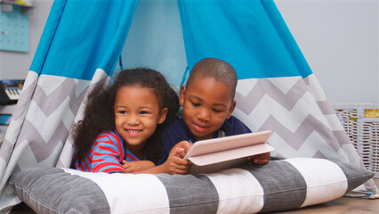 Two Children Lying In Tent In Playroom With Digital Tablet © Monkey Business