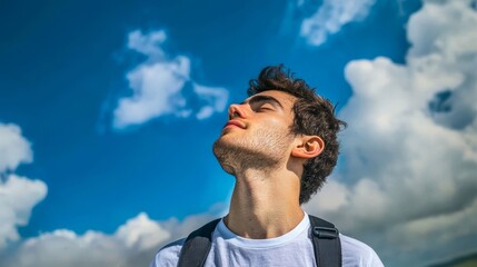 Young man enjoying the sunshine and feeling refreshed while traveling alone under a bright blue sky.
