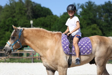 Smiling boy riding a pony during summer training session