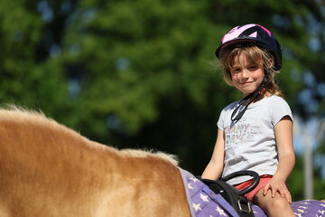 Smiling little girl riding a pony during summer training