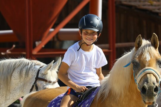 Smiling boy riding a pony at summer horse camp