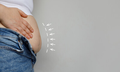 Female hand and belly close up on gray background. Weight loss and aesthetic surgery concept.