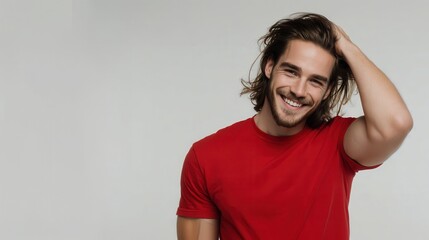 Confident young male model with flowing brown hair, wearing bright red tee, running fingers through hair and grinning against white backdrop