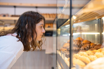 Caucasian woman looks greedily at baked goods in a bakery. 