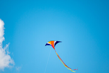 Single colorful kite flying high with long tail in clear blue sky