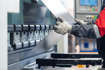 Male worker operating industrial metal press in factory setting
