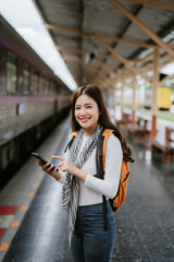A beautiful Asian female tourist smiling while using her phone at a train statio