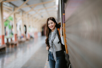 Fototapeta premium Young female traveler with small backpack at train station. 30s woman waiting for train. Travel. Solo leisure. Back view. No face.